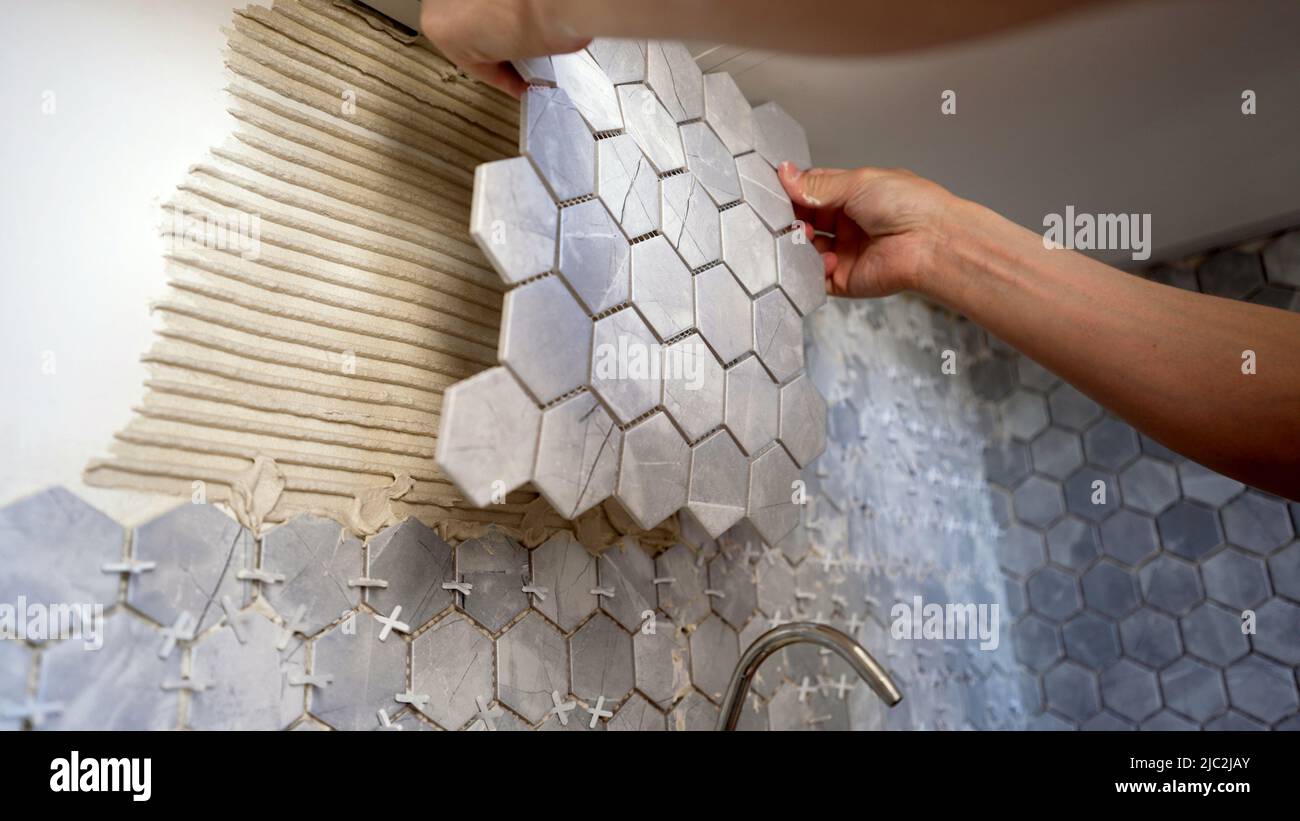 Le maître tient un carreau de mosaïque dans ses mains pour le coller sur le mur. Le carreleur tient une tuile entre ses mains. Le maître colle les carreaux sur le mur dans le TH Banque D'Images