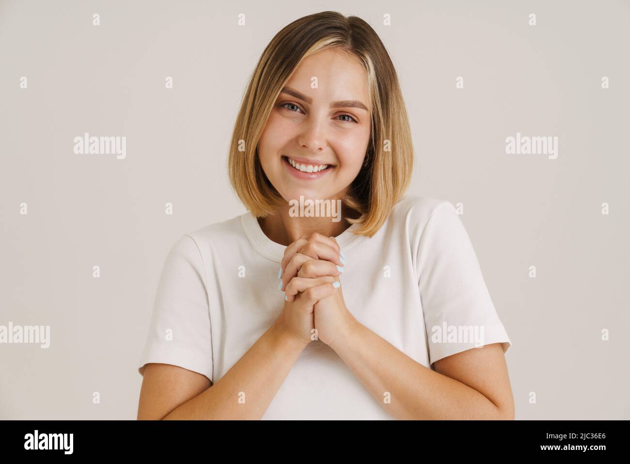 Jeune femme blonde souriant tout en tenant ses mains isolées sur fond blanc Banque D'Images