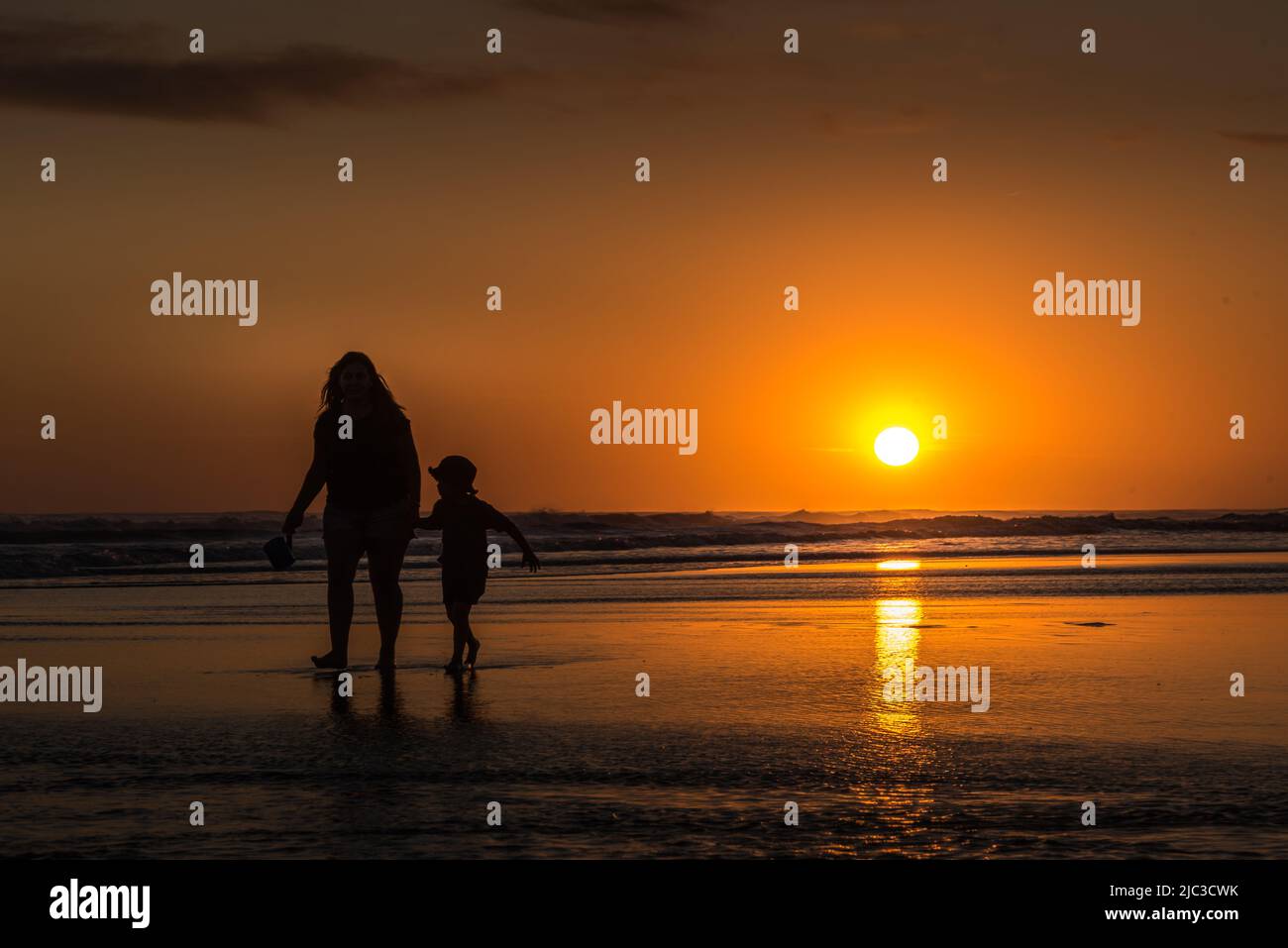 Forme de mère et d'enfant marchant sur la plage au coucher du soleil sur la mer et reflet sur l'eau Banque D'Images