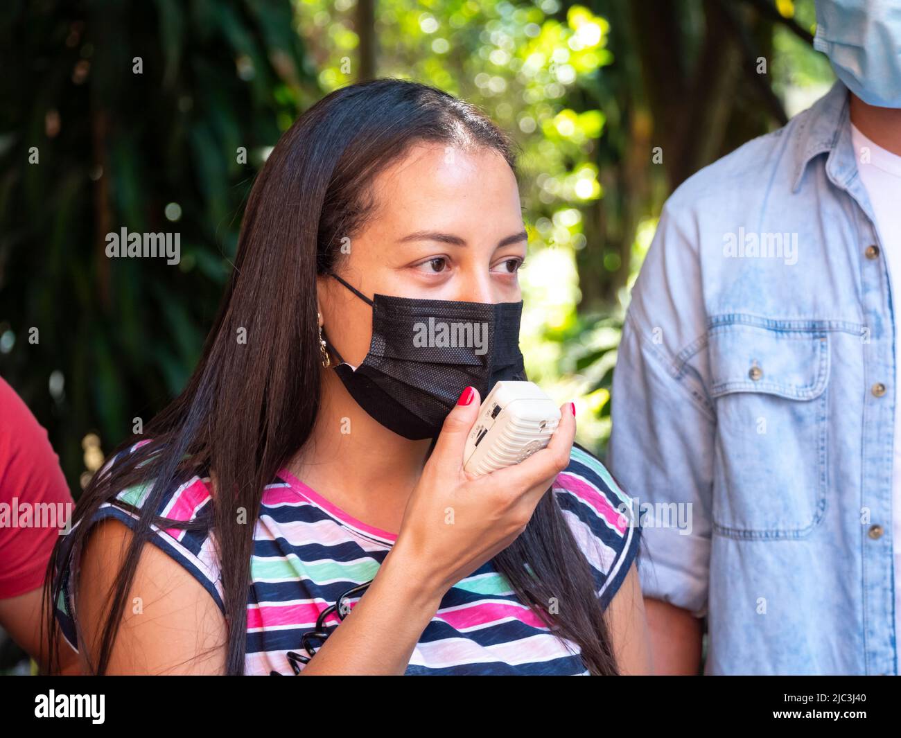 Medellin, Antioquia, Colombie - 19 février 2022: Jeune femme sud-américaine avec de longs cheveux bruns et masque de visage parle dans un mégaphone Banque D'Images
