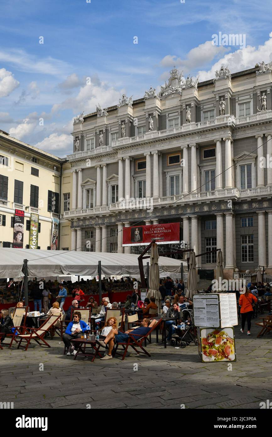 Personnes ayant des apéritifs dans un café pavé en face du Palais des Doges (Palazzo Ducale) avec les stands de la Foire du Livre à Piazza Matteotti, Gênes Banque D'Images