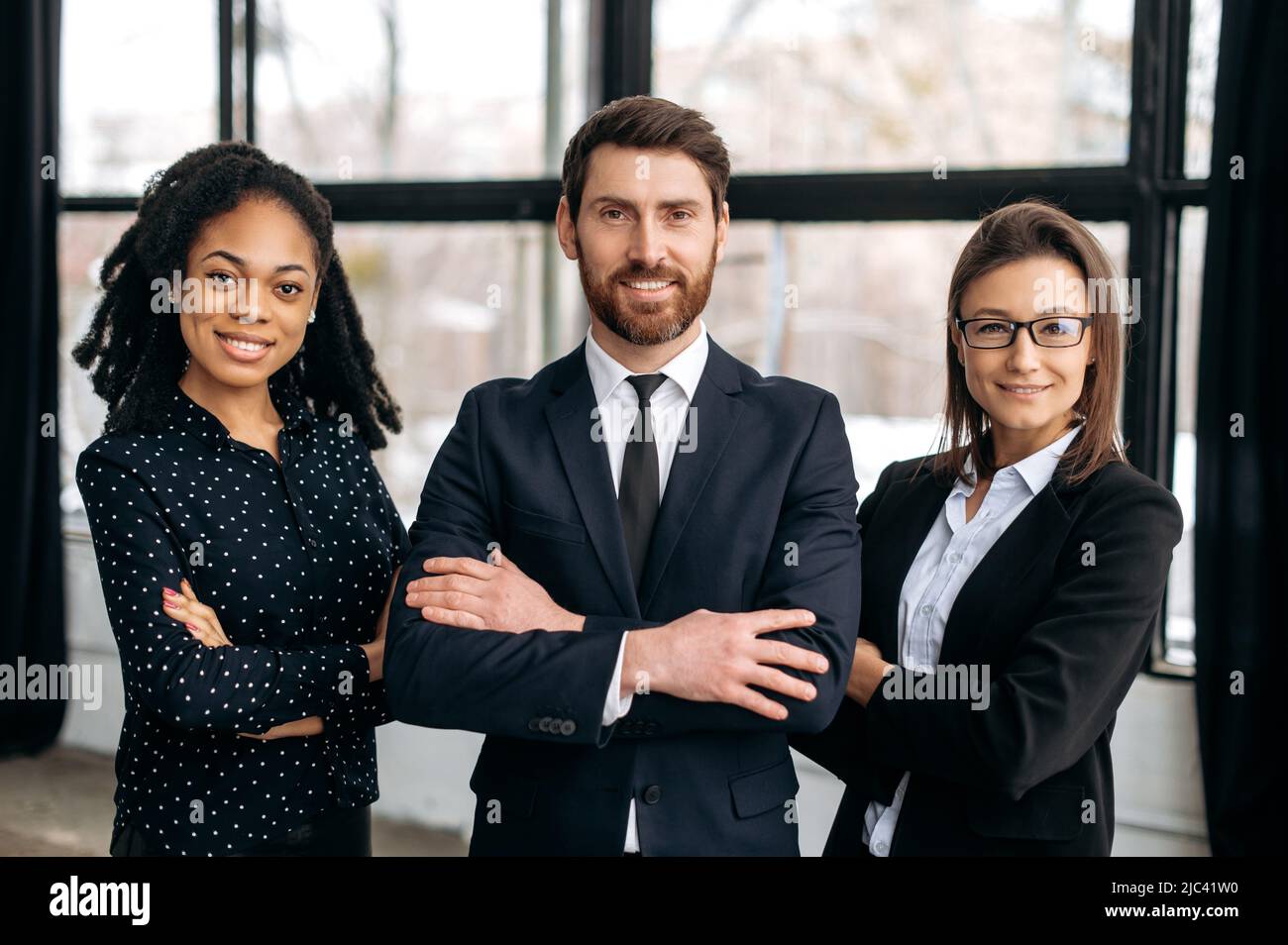 Portrait de groupe des partenaires d'affaires. Collègues multiraciaux à succès, vêtus de vêtements formels, debout dans leur bureau moderne avec leurs bras croisés, regardant la caméra, souriant amical Banque D'Images