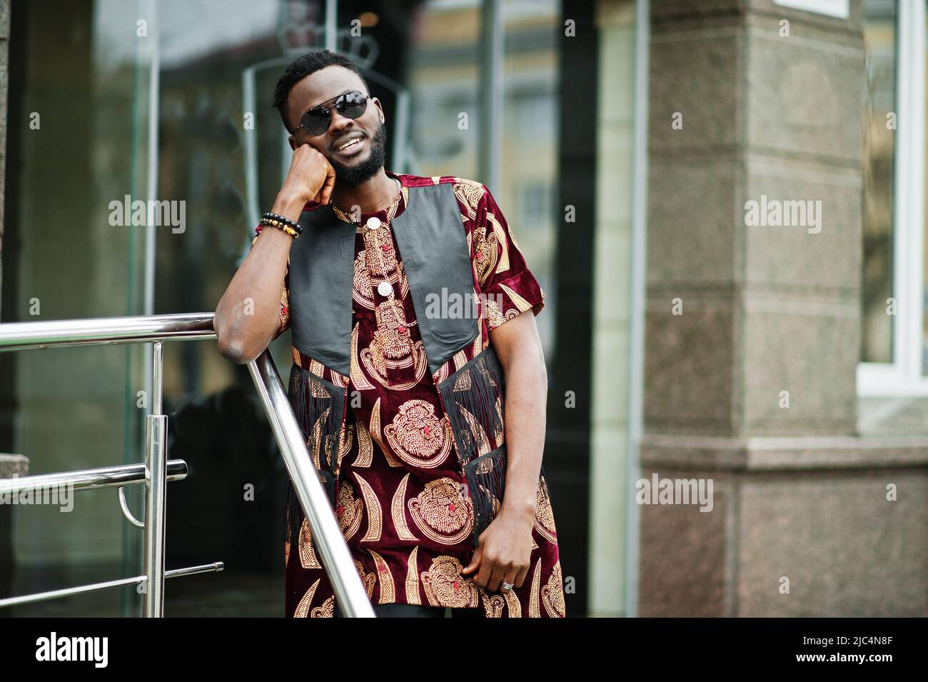 Homme africain élégant et beau dans une tenue traditionnelle et des lunettes de soleil debout à l'extérieur. Banque D'Images