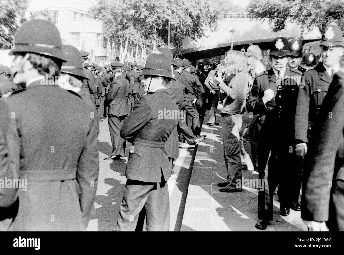 Marche du Front national (NF) d'extrême droite, Londres, Angleterre, Royaume-Uni, entourée de policiers, septembre 1978. Le même jour, une marche de la Ligue anti-nazie a eu lieu à Londres, de sorte que la police était là en grand nombre pour garder les deux marches séparées et pour faire face à tout conflit entre elles. Une image de nombreux hommes en uniforme sombre ensemble, avec peut-être 5 hommes non-uniformes à peu près visibles, difficile de voir les manifestants NF dans cette phalange de policiers ; certains policiers avaient les cheveux longs (premier plan gauche). Prise sur un appareil photo rétro 35mm sur film noir et blanc, probablement Ilford FP4 film. Banque D'Images