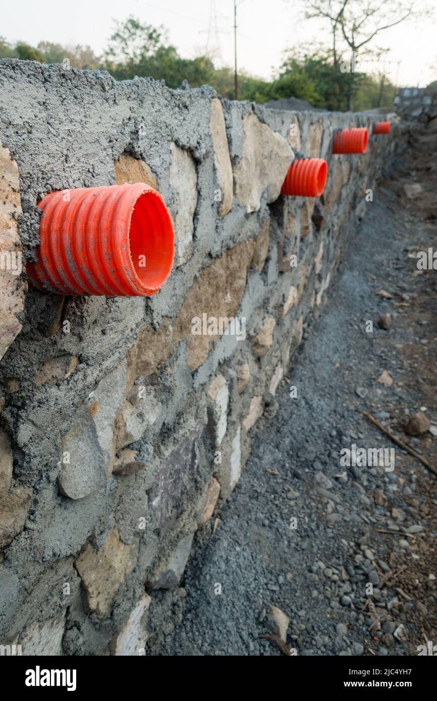 Une rangée de ponceaux orange ou de tuyaux de sortie d'eau à travers un mur de retenue en pierre pour le drainage des tempêtes dans les collines d'Uttarakhand Inde. Banque D'Images