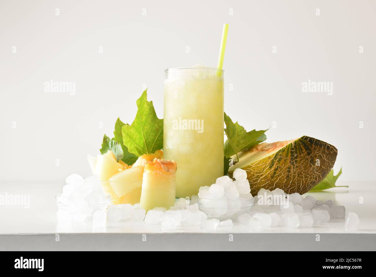 Melon sluschie dans un grand verre de fruits et glace pilée autour de lui sur table blanche avec fond isolé. Vue avant. Composition horizontale. Banque D'Images
