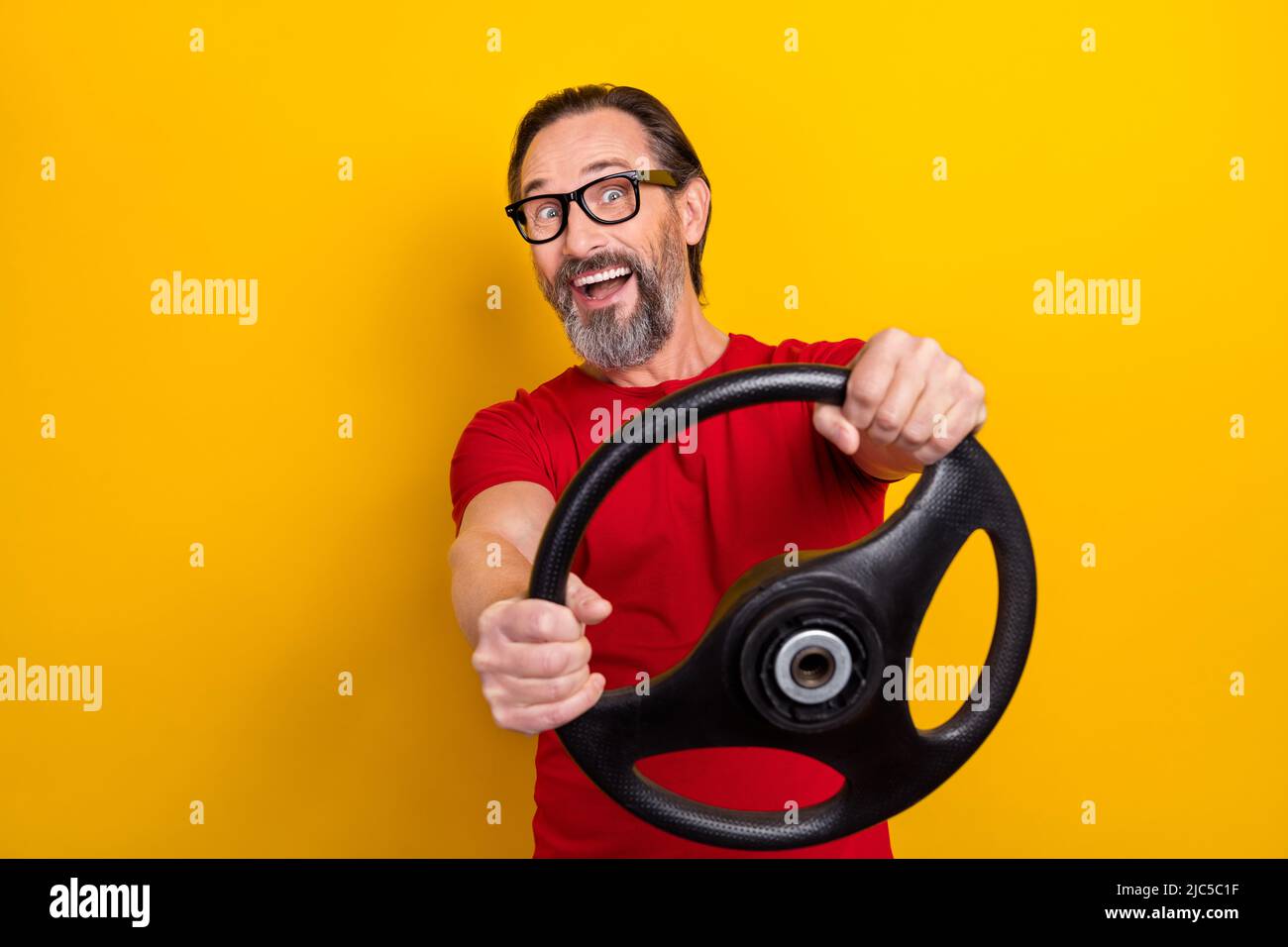 Photo de joli impressionné homme retraité porter des lunettes t-shirt rouge équitation voiture sourire isolé couleur jaune fond Banque D'Images