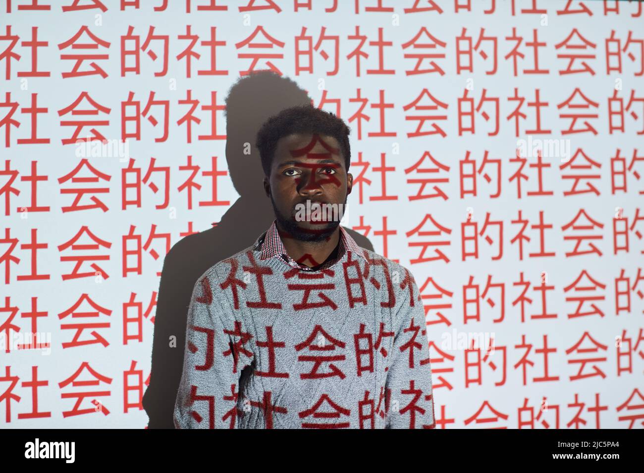 Jeune homme noir sérieux avec barbe debout contre l'écran de projection avec des symboles chinois rouges Banque D'Images