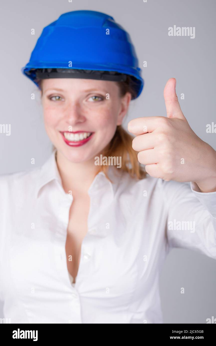 Une jeune femme ingénieure portant un casque bleu fait quelques gestes et montre le pouce vers le haut Banque D'Images