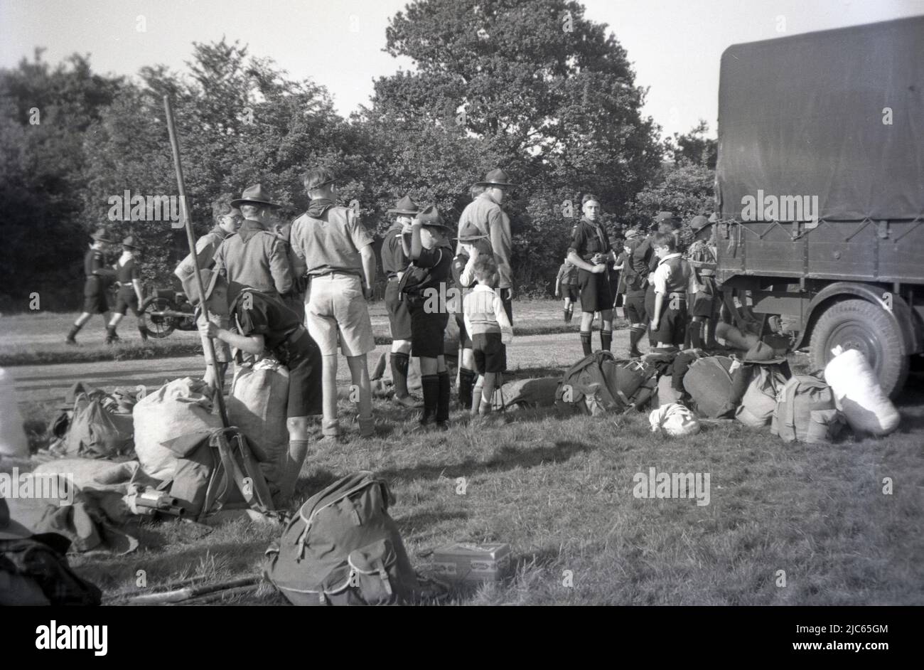 1937, historique, se remballer après un camp de scouts à Ranmore Common, Dorking, Surrey, Angleterre, Royaume-Uni. Des scouts en uniforme et des scouts de garçon debout à côté des sacs à dos de toile de l'époque, emballés et prêts à aller dans le camion d'attente. Banque D'Images