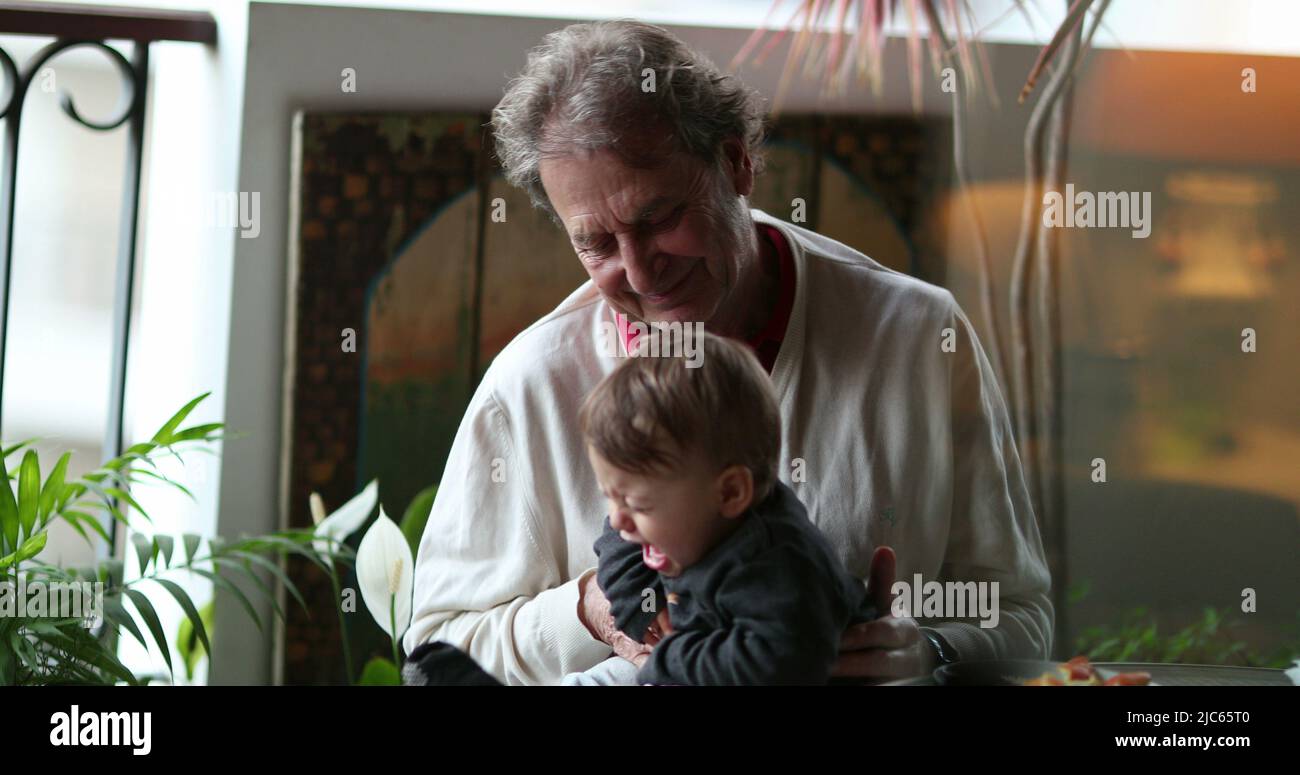 Grand-père décontracté avec bébé petit-fils à la maison balcon, choqué pleurs bébé garçon avec grand-père genoux Banque D'Images