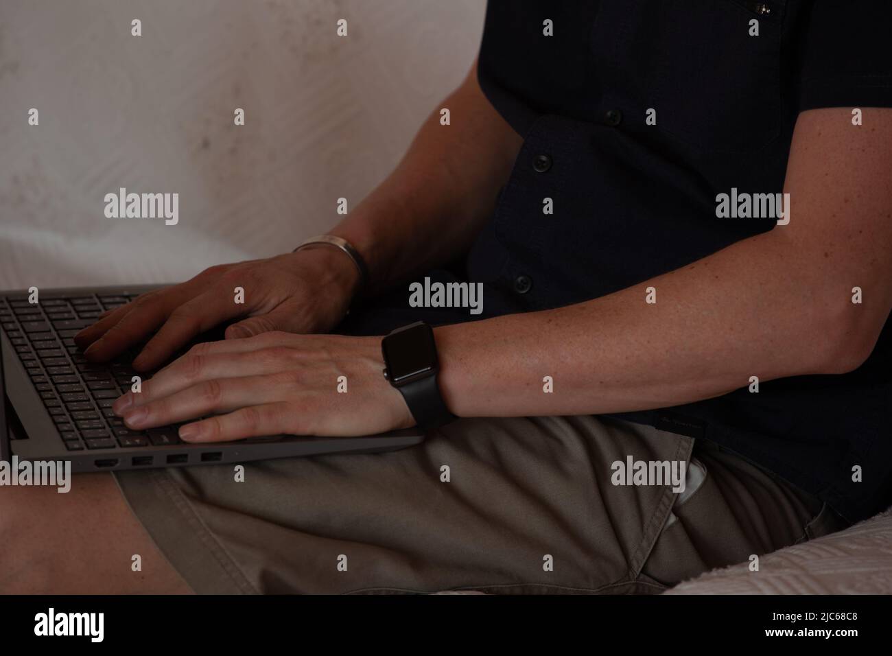 les mains d'un homme sur un clavier d'ordinateur. un homme à la peau blanche tape sur les touches d'un clavier d'ordinateur portable. Il est assis sur un canapé blanc. Nous ne pouvons pas voir son visage Banque D'Images