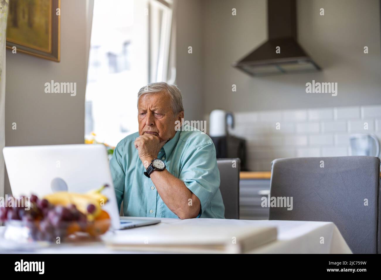Homme âgé utilisant un ordinateur portable à la table de cuisine Banque D'Images