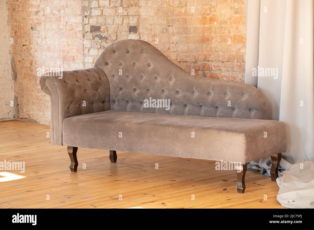 un fauteuil rembourré gris portait un mur brun en brique dans un appartement sur un plancher en bois, des meubles rembourrés à la maison, design et intérieur Banque D'Images