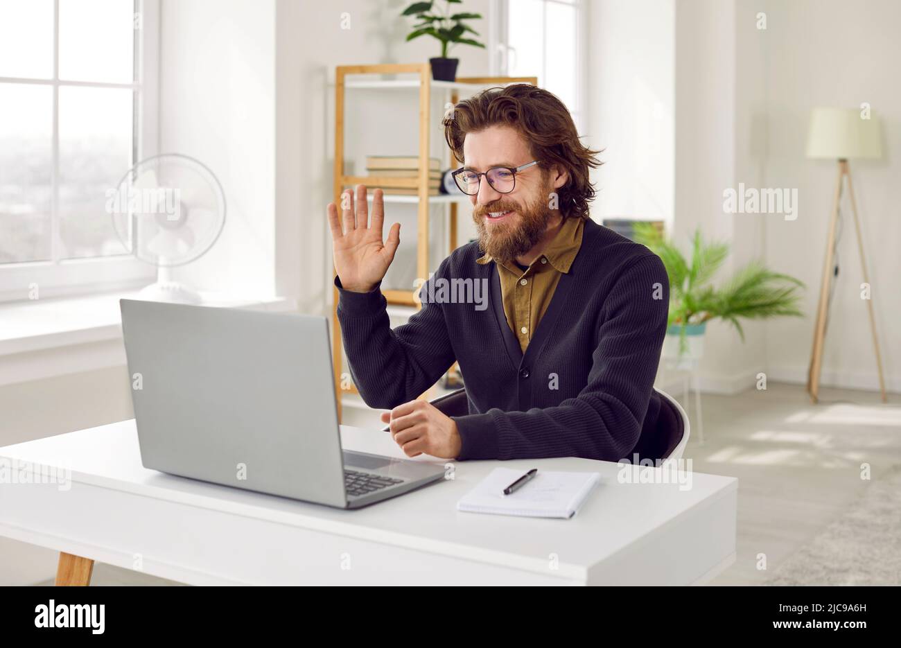 Heureux homme assis au bureau avec ordinateur portable, commencer la réunion en ligne et de saluer Banque D'Images
