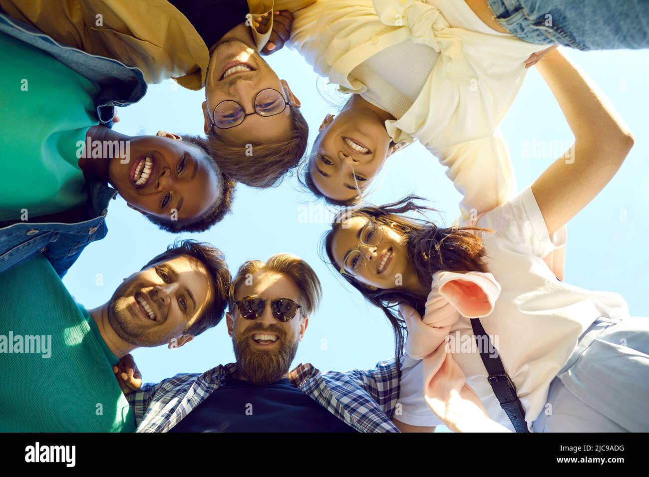 Groupe de jeunes amis multiraciaux heureux et joyeux qui se embrasse, regardent vers le bas et sourient Banque D'Images