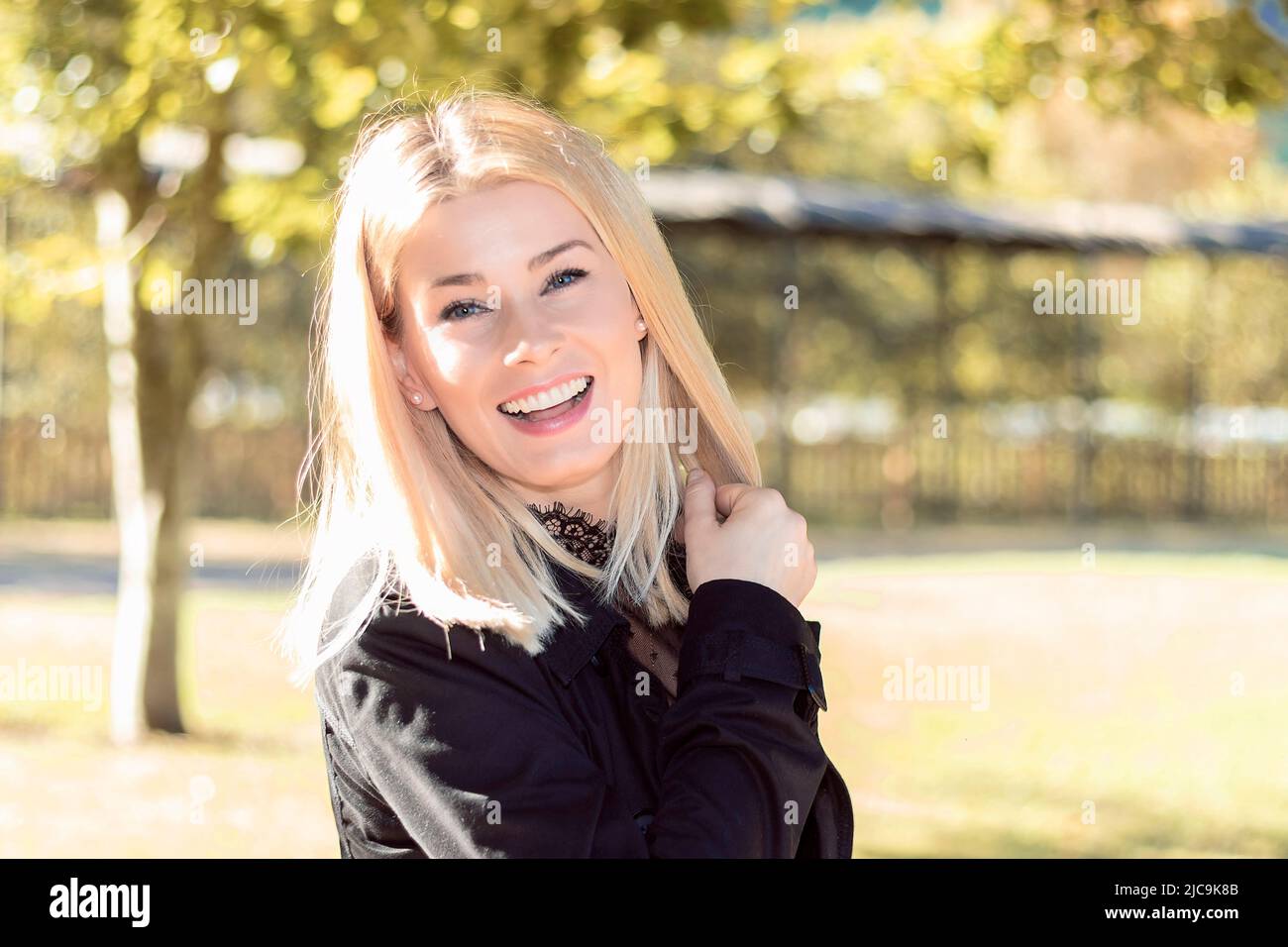 jolie femme blonde souriante dans un parc habillé de noir Banque D'Images