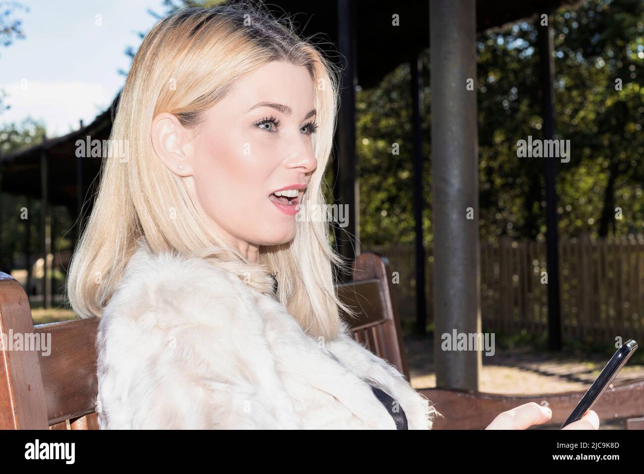 femme blonde assise dans un parc avec un mobile Banque D'Images