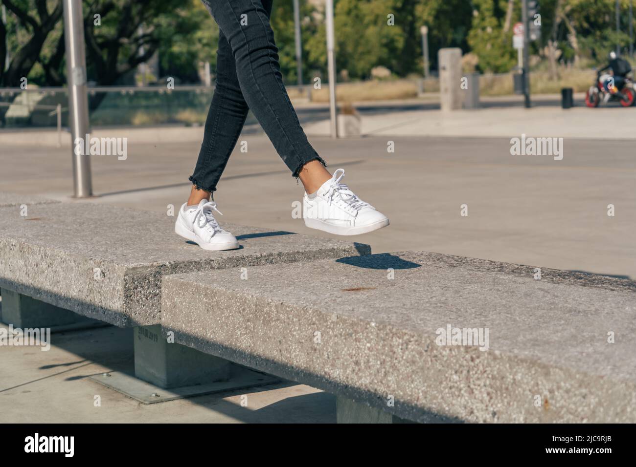 Les jambes fines des sneakers blanches sautent entre des blocs de béton dans un carré. Concept drôle de temps. Banque D'Images