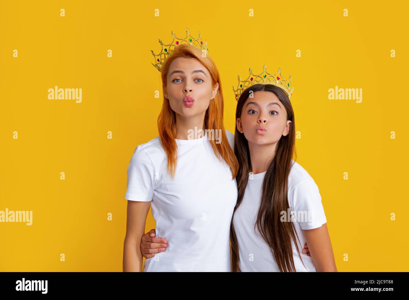Mère et fille gaies portant la couronne lors d'une fête familiale. Filles drôles avec couronne, arrière-plan isolé. Banque D'Images