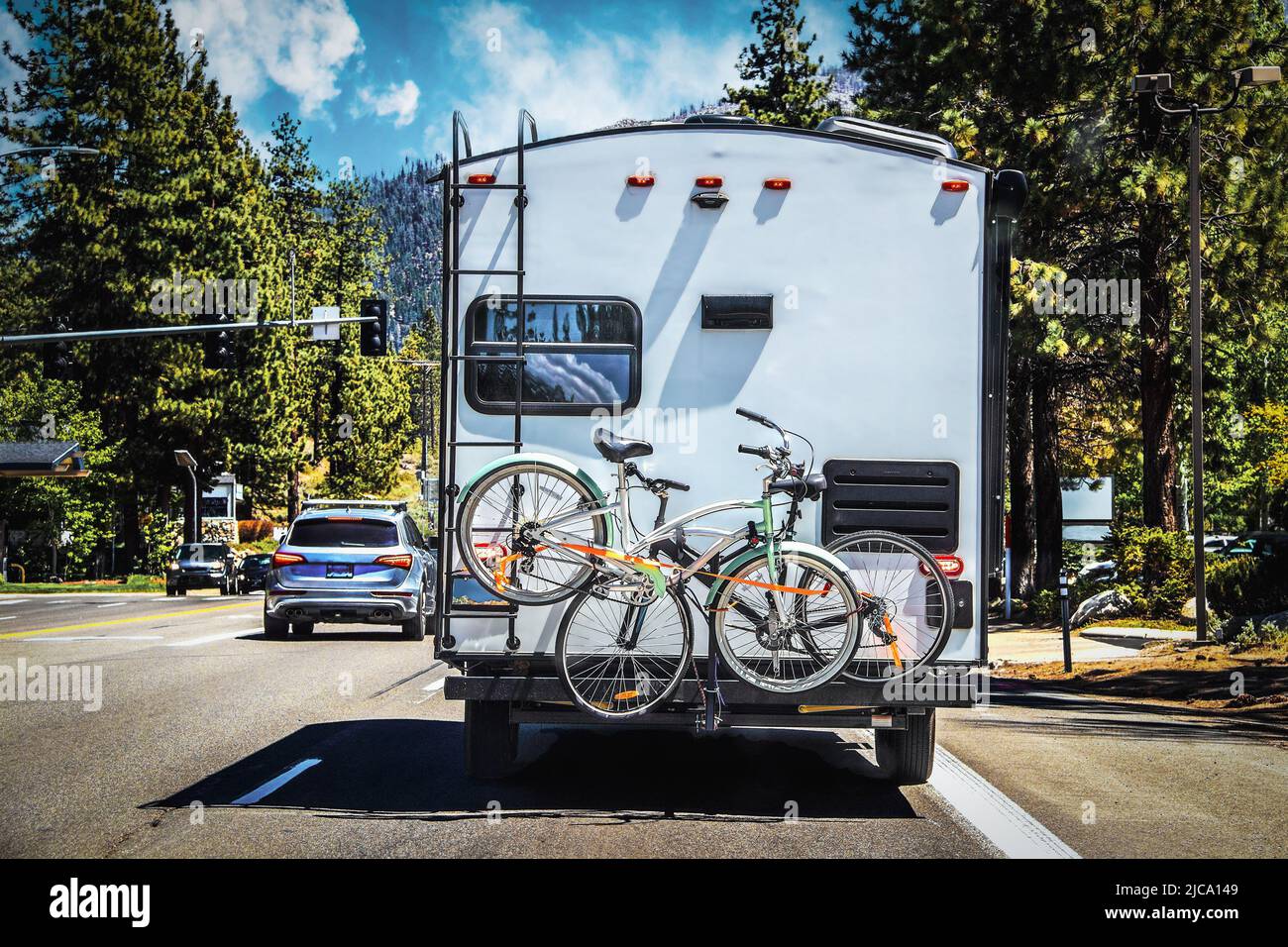 Campeur avec deux vélos attachés à l'arrière sur l'autoroute bordée d'arbres à l'extérieur du lac Tahoe avec des montagnes à distance sur le soleil de l'été da Banque D'Images
