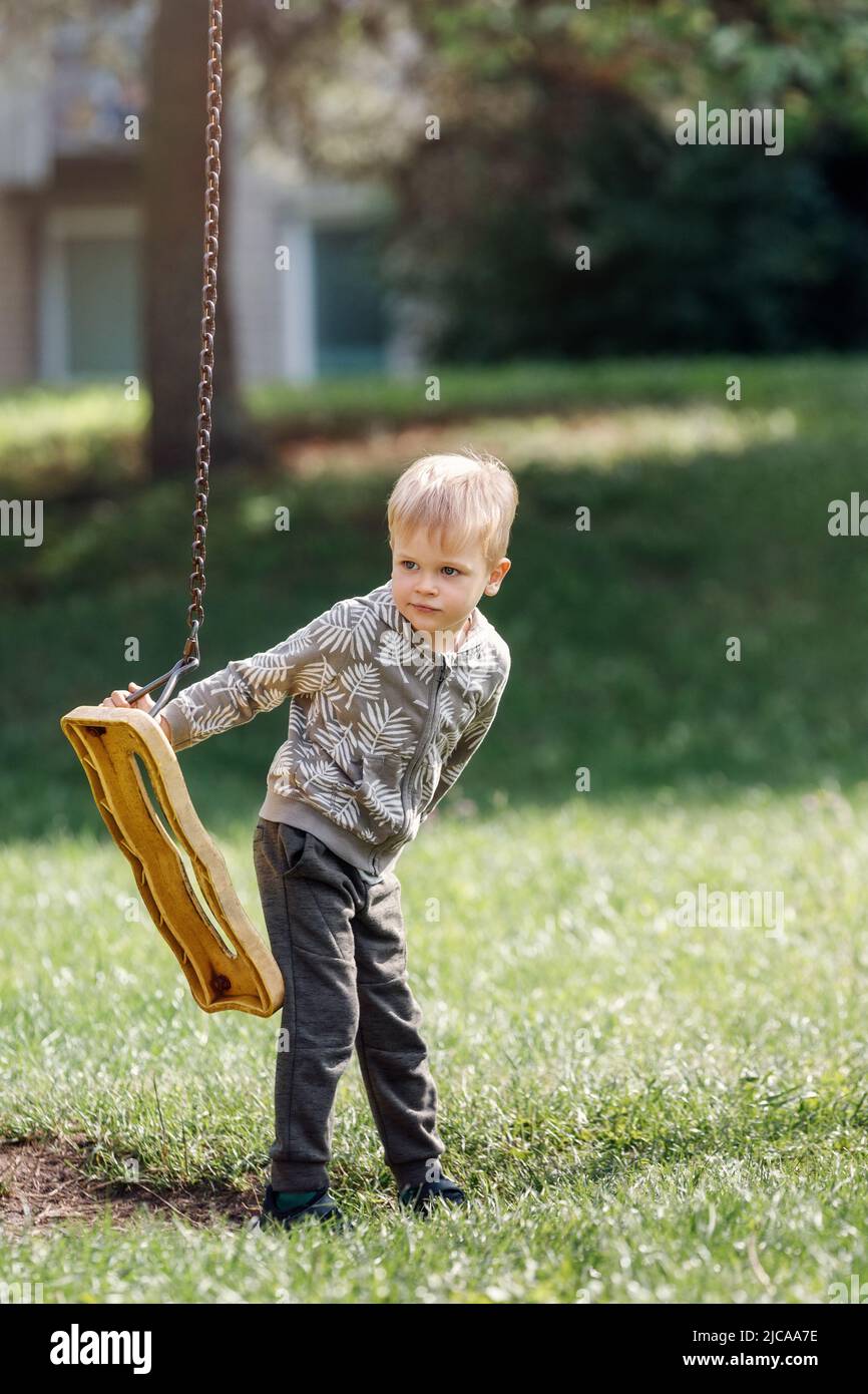 Une balançoire cassée dans un parc de la ville et un adorable garçon qui ne peut pas balancer. Banque D'Images