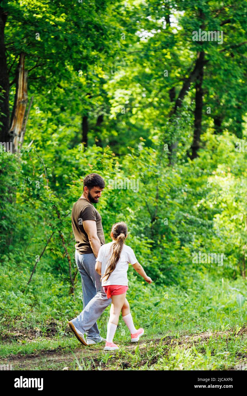 Vue arrière de la famille marchant dans la forêt du parc autour des arbres, parlant, s'amuser. Activités d'été, voyages. Verticale. Banque D'Images