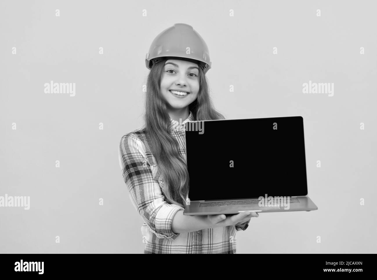 jeune fille dans le casque présentant ordinateur portable. ordinateur de garde d'enfant de constructeur. bâtiment et construction. Banque D'Images