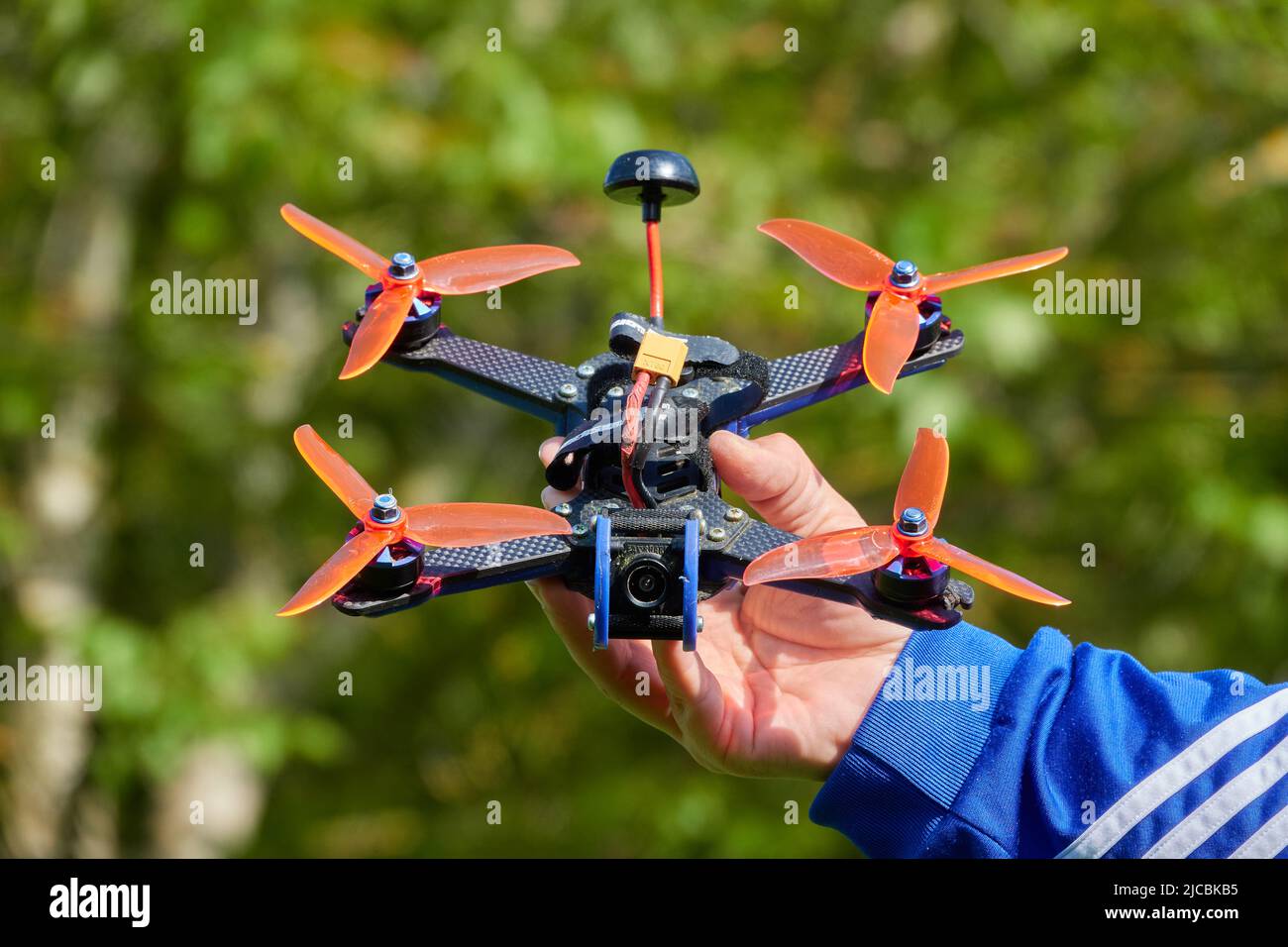 Nuertingen, Allemagne - 16 mai,2020: Le drone noir également la course quad, avec orange hélice, est tenu par des mains humaines. Herbe floue en arrière-plan. Allemagne Banque D'Images