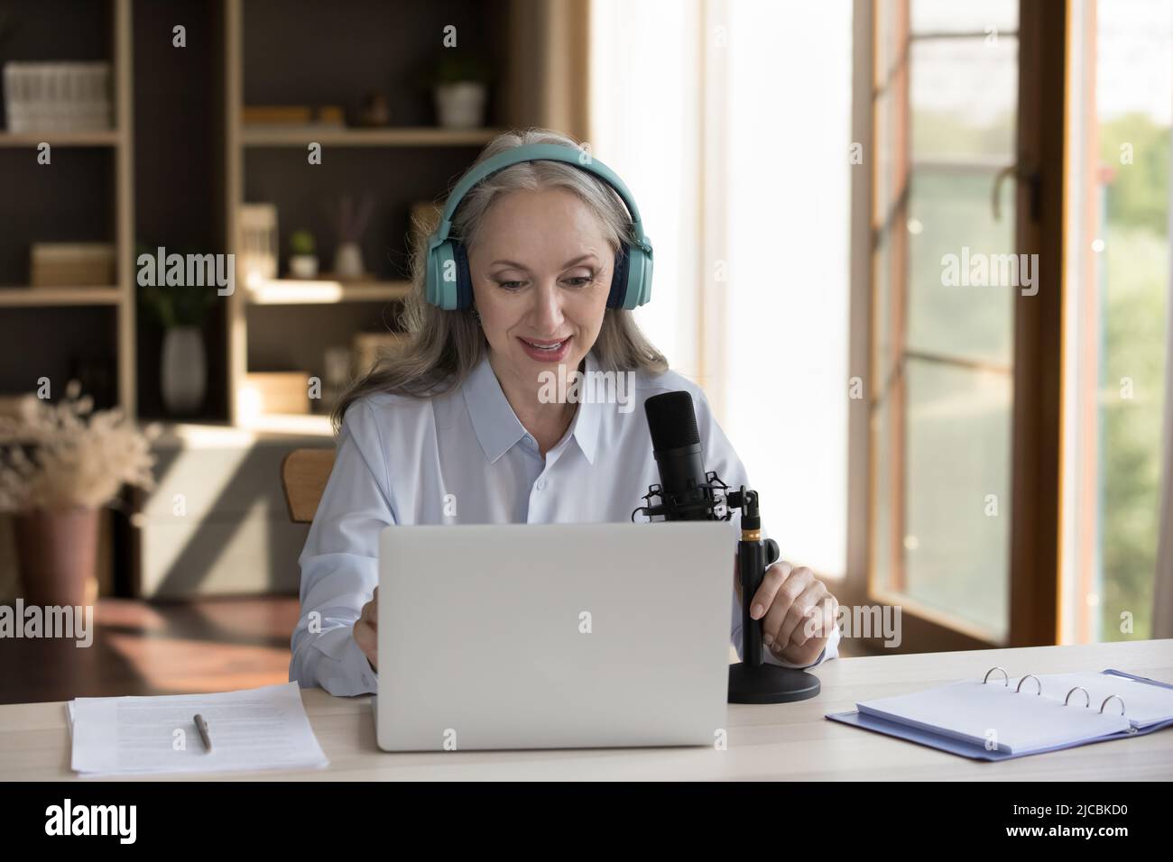 Une femme plus âgée parlant dans un micro s'assoit au bureau avec un ordinateur portable Banque D'Images