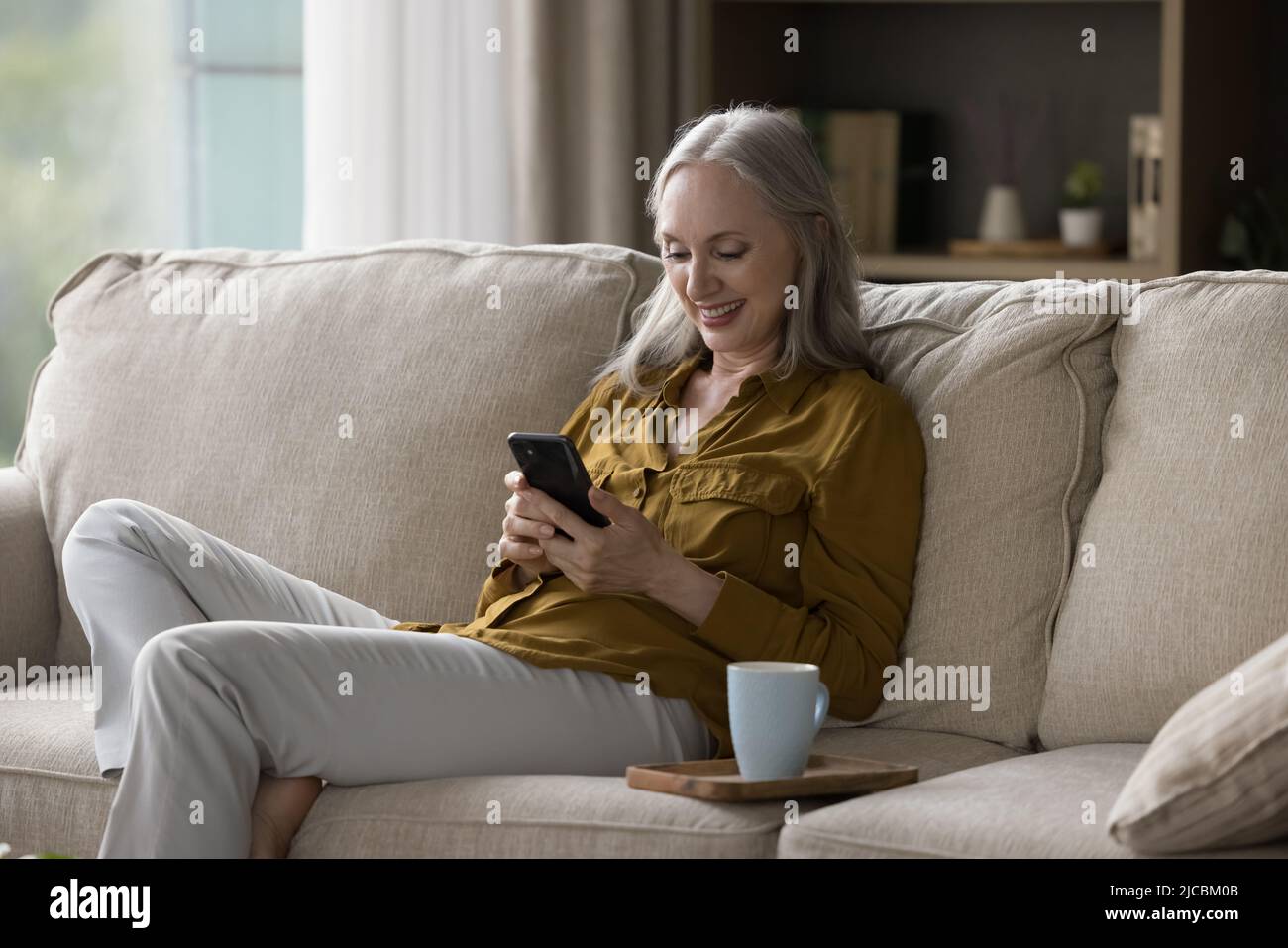 Bonne femme âgée se reposant sur un canapé avec un smartphone Banque D'Images
