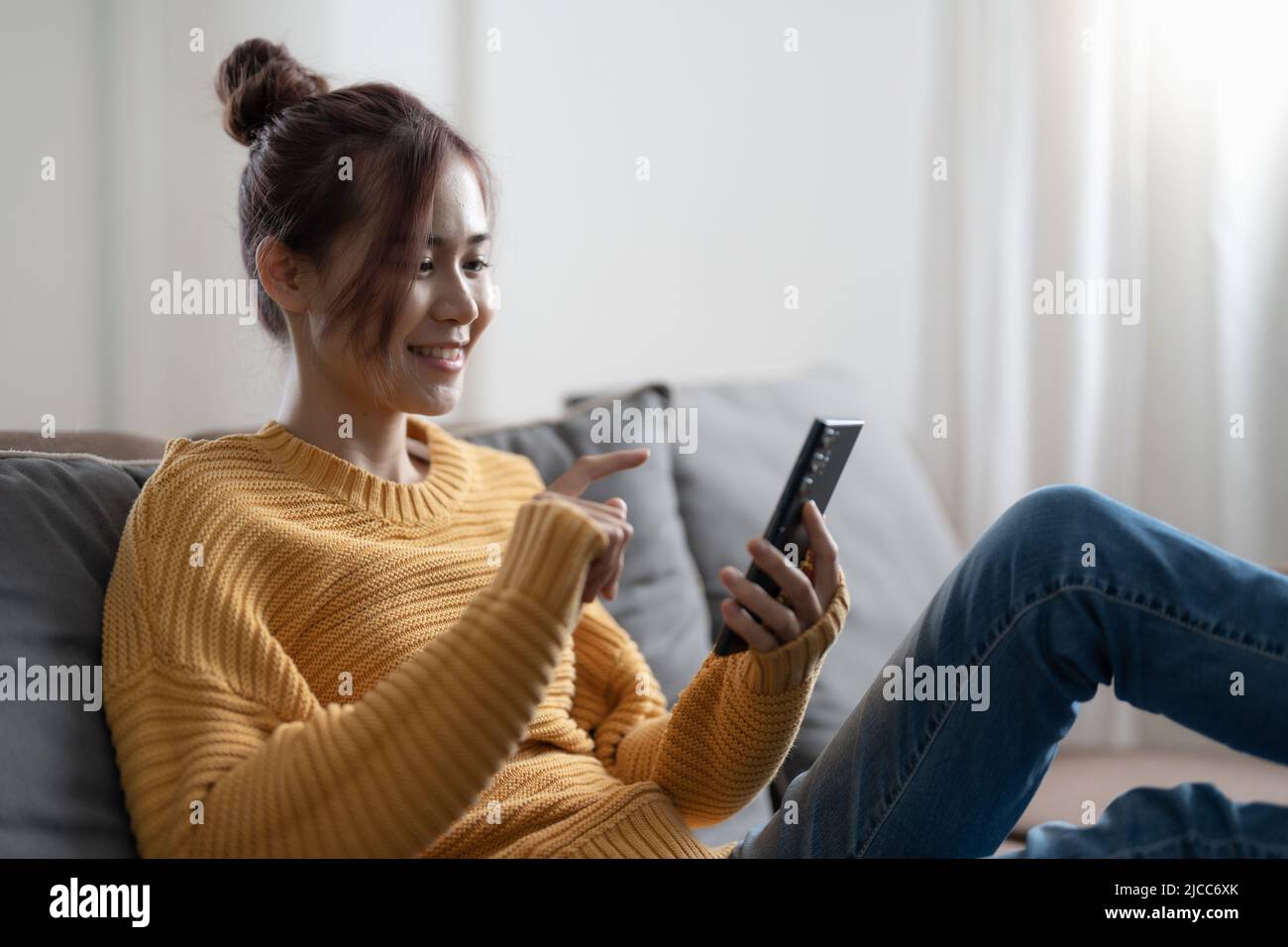 Bonne fille asiatique de l'adolescence vérifier les médias sociaux tenant le smartphone à la maison. Jeune femme souriante utilisant l'application de téléphone mobile jouant à des jeux, magasiner en ligne Banque D'Images