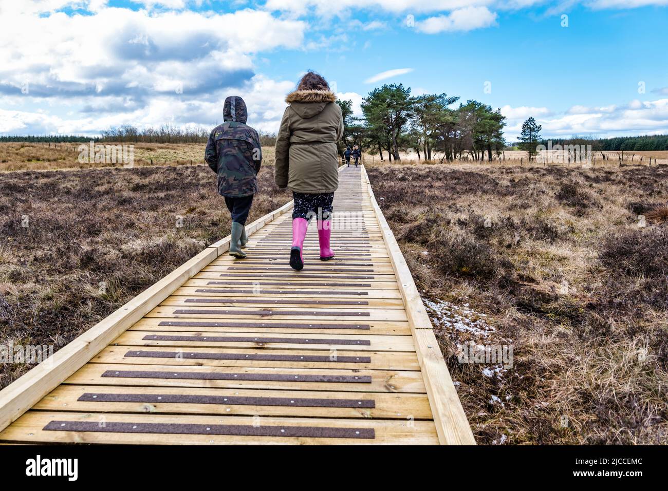 Personnes marchant sur une promenade en bois portant des bottes Wellington à la réserve naturelle nationale de Blawhorn Moss, West Lothian, Écosse, Royaume-Uni Banque D'Images