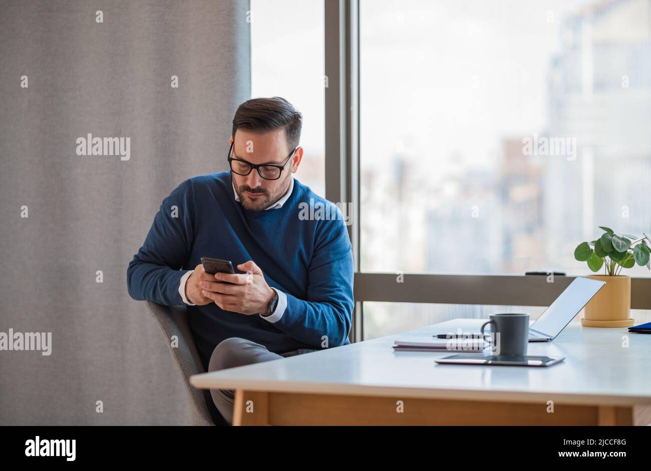 Messages en ligne pour jeunes entrepreneurs masculins sur téléphone mobile. Homme d'affaires travaillant sur un ordinateur portable au bureau. Il porte des vêtements décontractés au bureau. Banque D'Images
