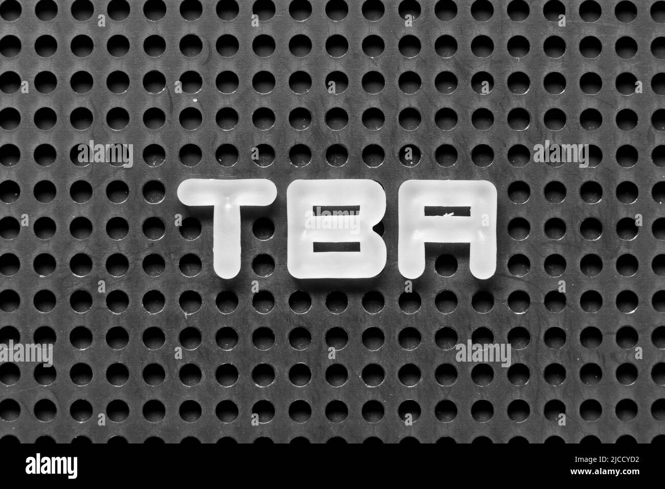 Lettre alphabétique blanche dans le mot TBA (abréviation de à annoncer) sur fond perforé noir Banque D'Images