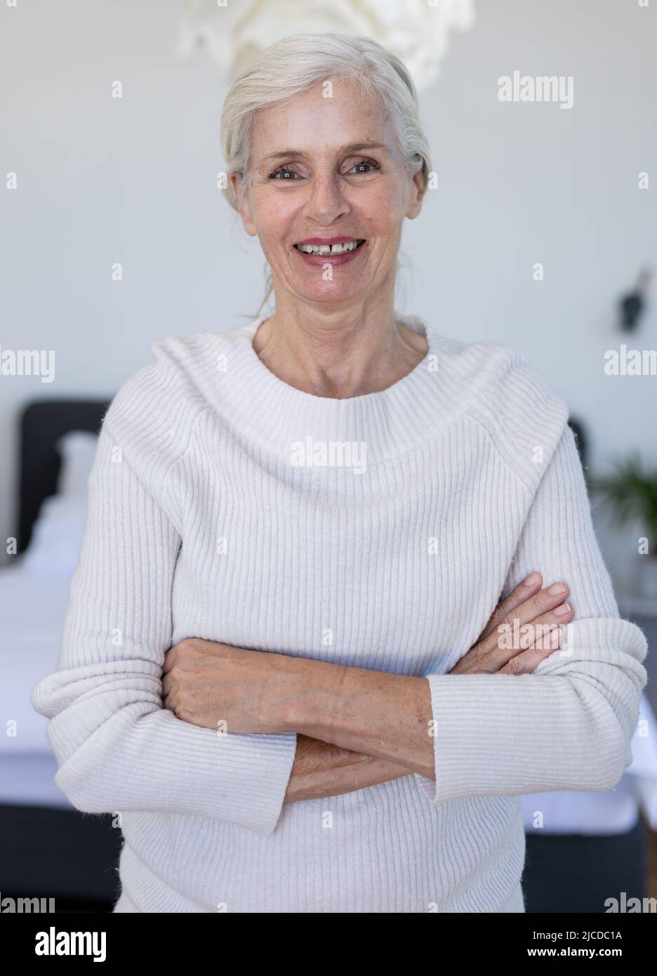 Portrait d'une femme de race blanche aux bras croisés souriant debout dans la chambre à la maison Banque D'Images