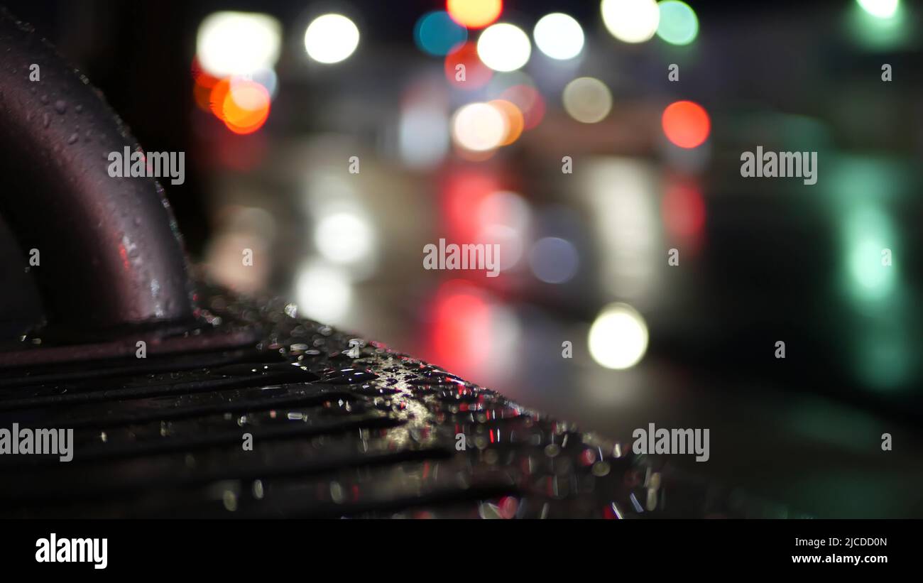 Feux de circulation de voiture bokeh, réflexion sur le banc d'arrêt de bus par temps pluvieux. Pluie d'eau tombe sur métal humide, rue de ville à Clifornia, Etats-Unis. Précipitations la nuit. Cinemagraph sans couture, abstrait et désoqué Banque D'Images