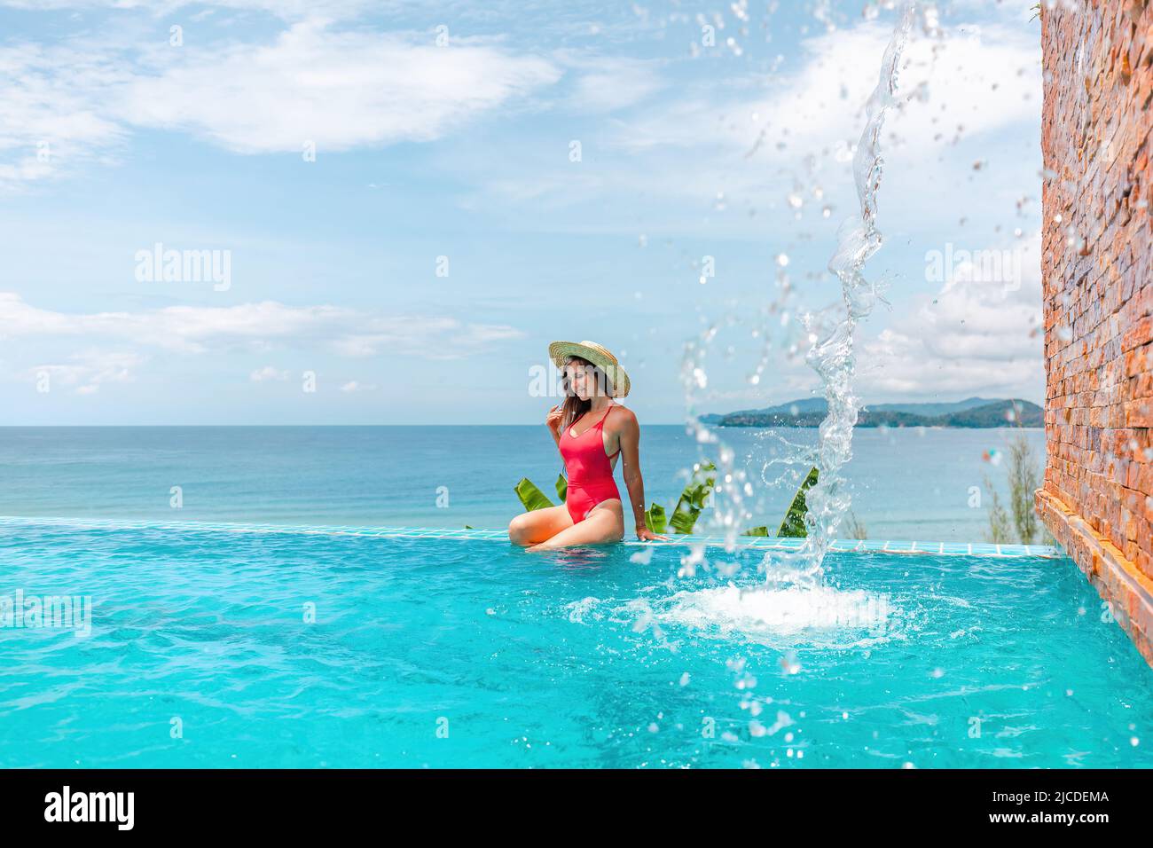 Vacances d'été avec vue sur la mer. Jeune femme en maillot de bain assis au bord de la piscine Banque D'Images