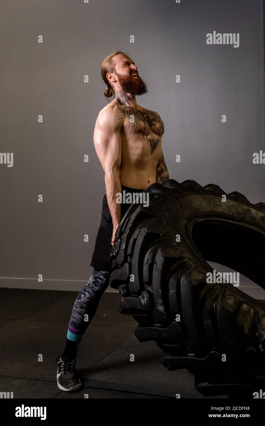 Fitness flipping crossfit jeune entraînement roue pneu gym forte poussée, pour l'entraînement de force pour la forme et l'athlète caucasien, paper bodybuilder. Pleine énergie Banque D'Images