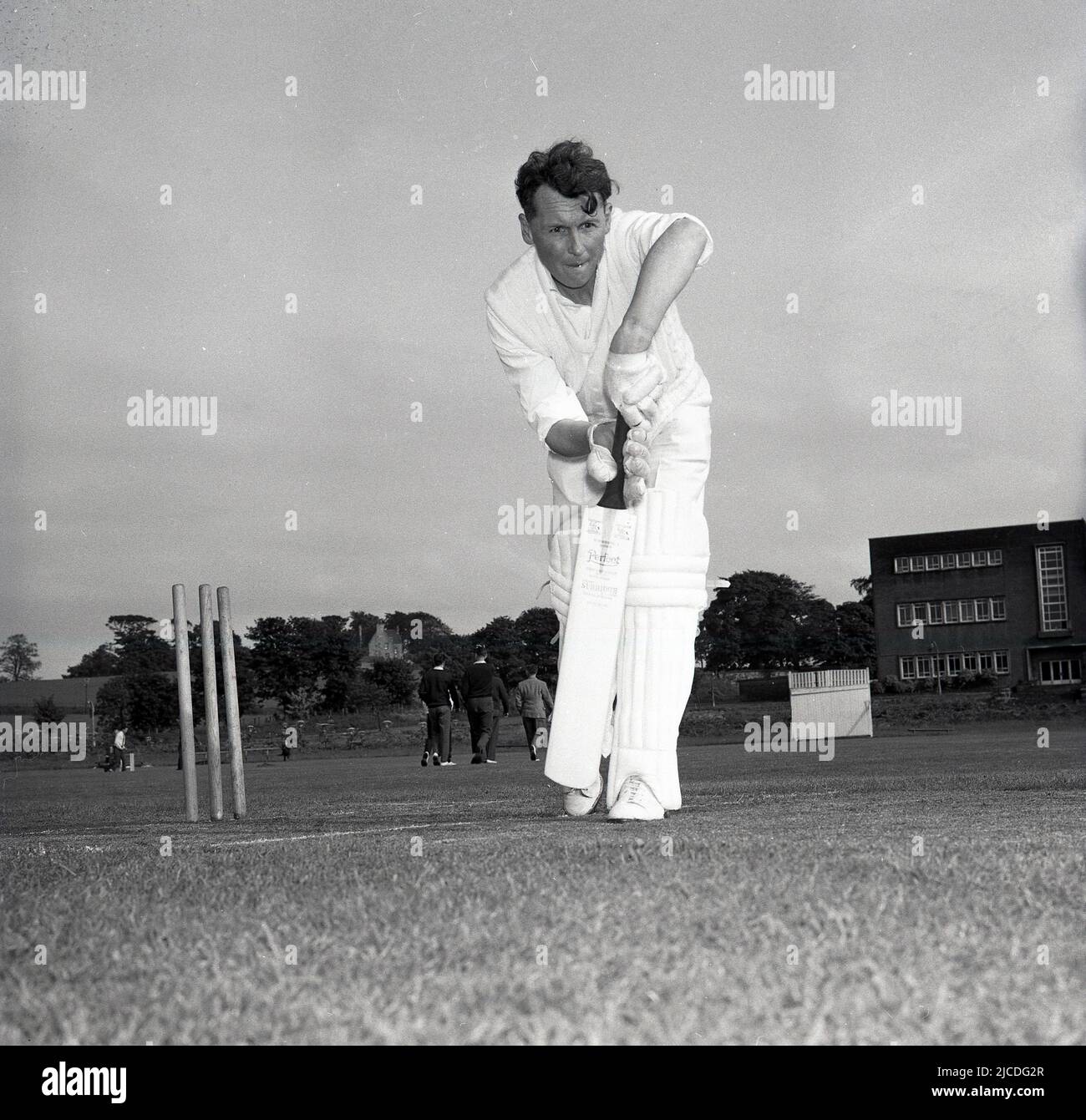 1960s, historique, un cricketeur amateur au pli devant ses bickets démontrant une presse avant avec sa chauve-souris et ses pads. Banque D'Images