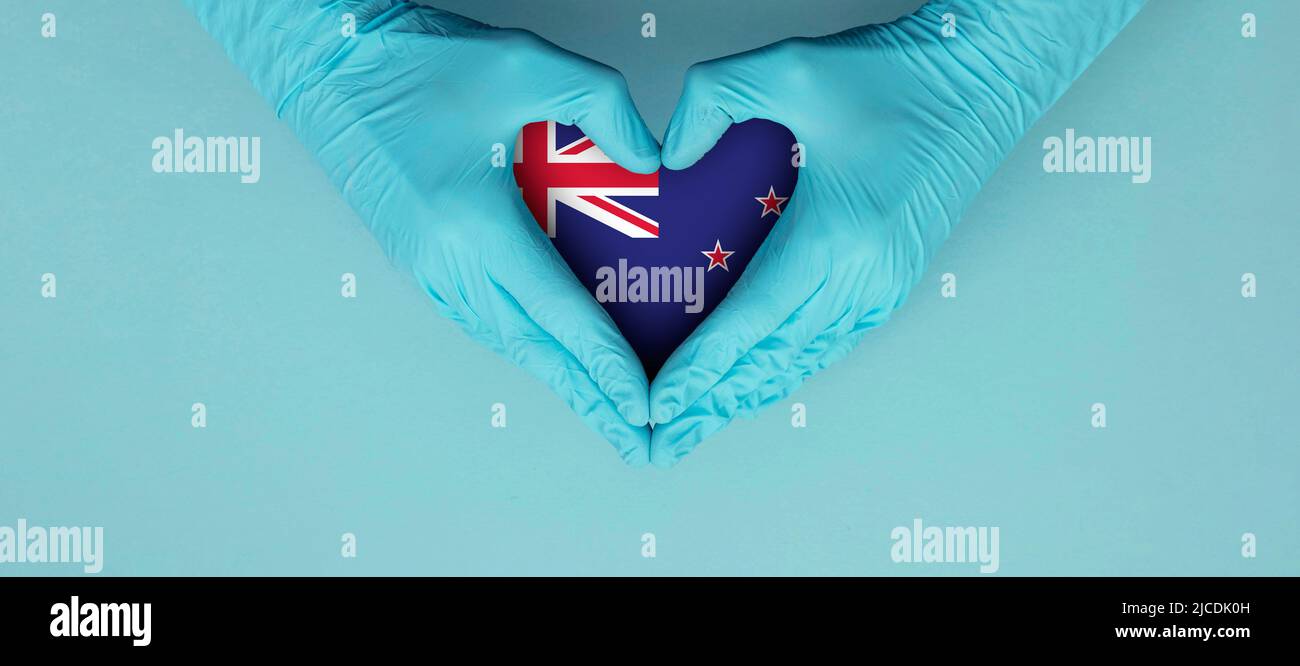 Les mains des médecins portant des gants chirurgicaux bleus faisant entendre le symbole de forme avec le drapeau de la nouvelle-zélande Banque D'Images