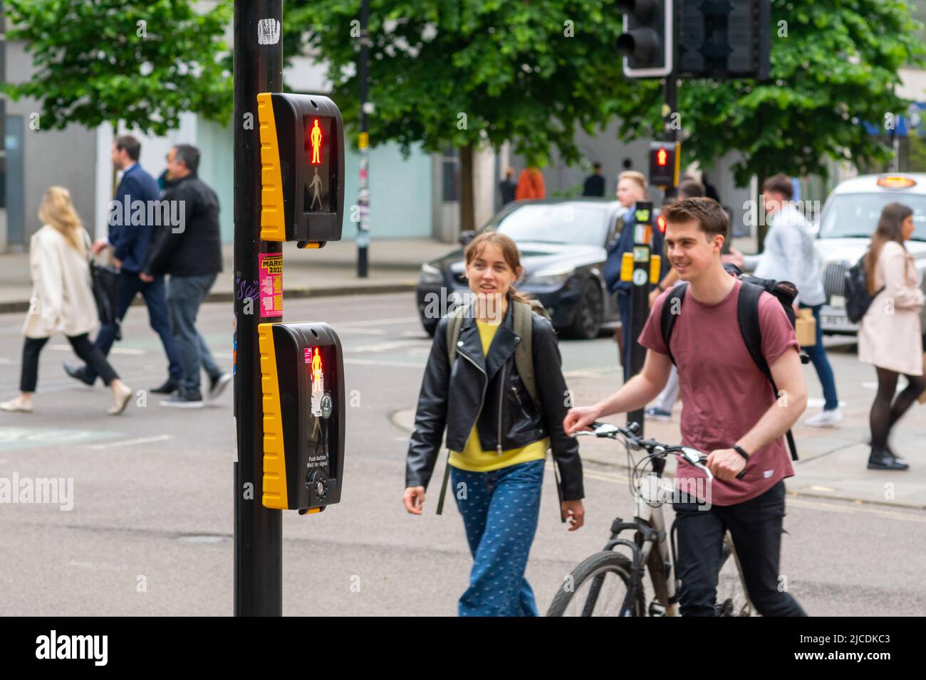 Deux personnes franchissent Market St à Manchester, au Royaume-Uni, tandis qu'un macareux affiche « homme d'origine » (ne pas traverser). Il n'y a pas de loi contre le passage en rouge Banque D'Images