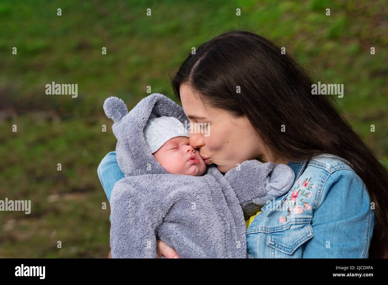 J'aime maman avec Newborn son sur ses bras à Spring Park. Сareful Mummy Kissing à l'adorable sommeil de l'enfant nouveau-né. La famille passe du temps ensemble sur la nature ou Banque D'Images