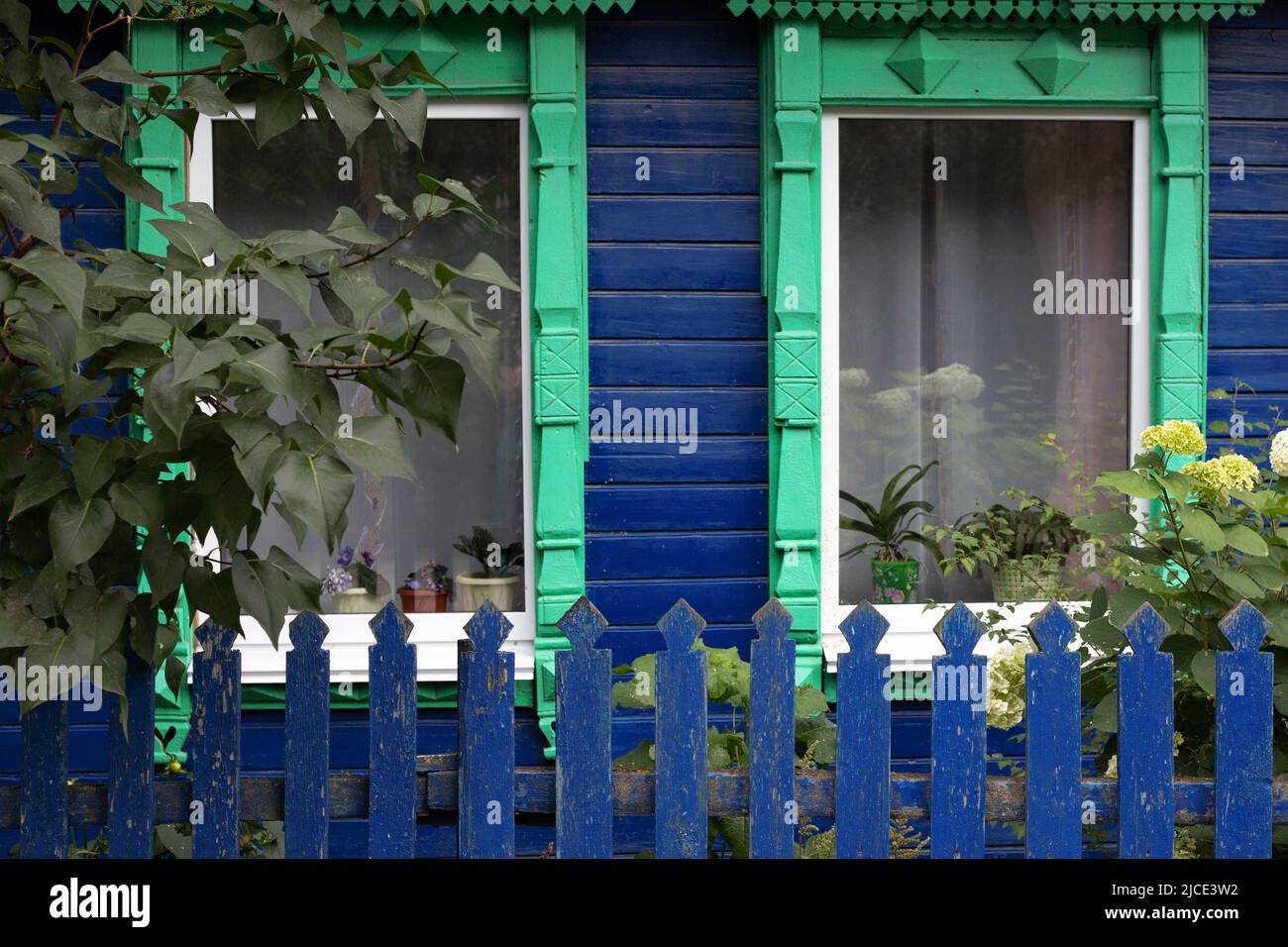 Fenêtres en platine sculptées vertes avec rideaux d'ancienne maison russe traditionnelle en bois peint bleu Banque D'Images