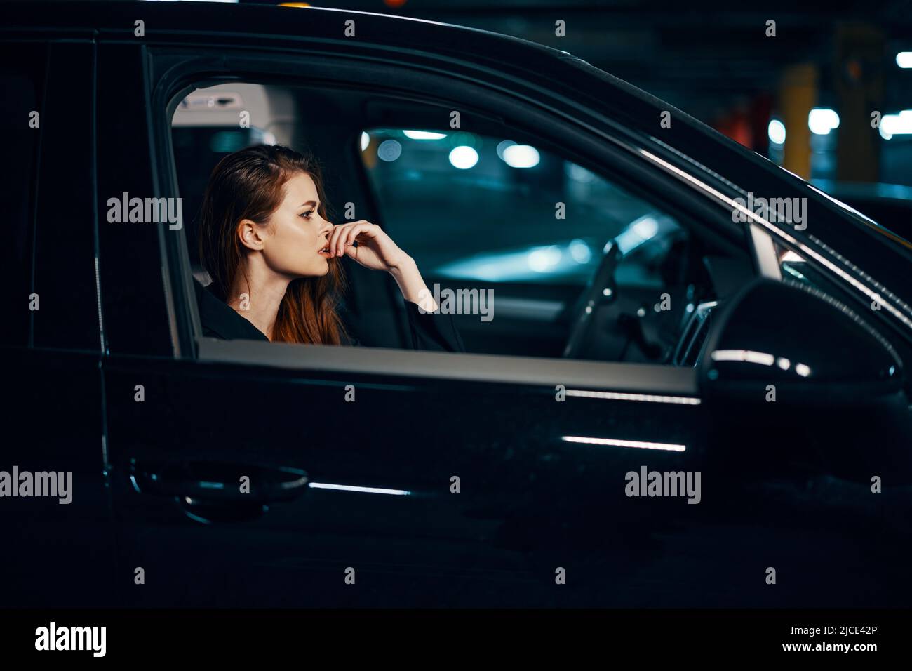 photo horizontale du côté, la nuit, d'une femme assise dans une voiture noire et regardant avec soin vers l'avant en tenant sa main près de son visage Banque D'Images