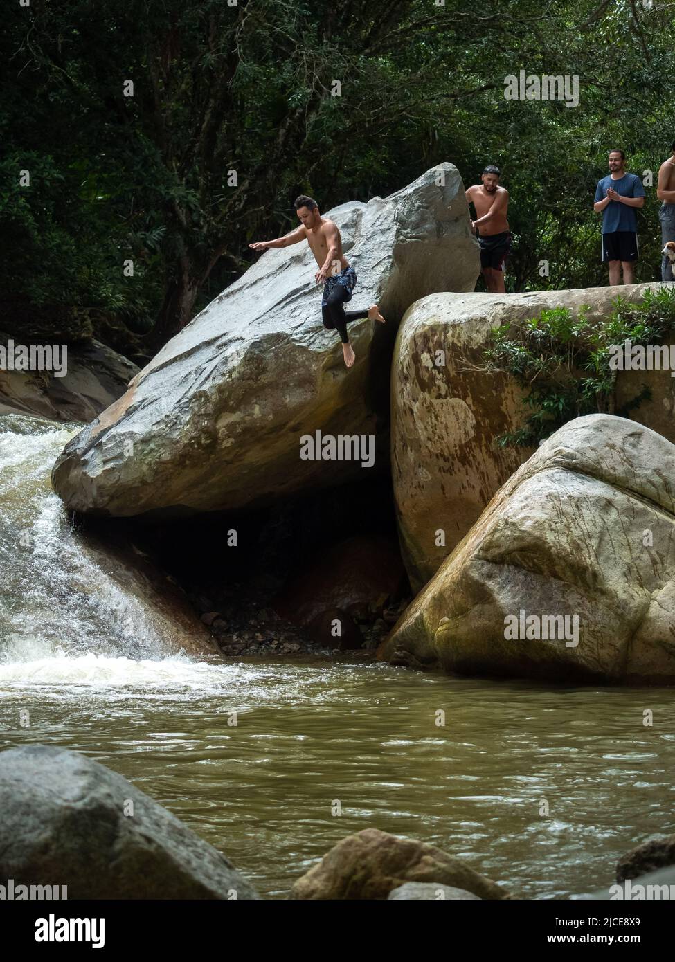 Cisneros, Antioquia, Colombie - 20 février 2022: Homme d'Amérique du Sud qui saute dans la rivière de grands rochers au milieu d'une forêt Banque D'Images