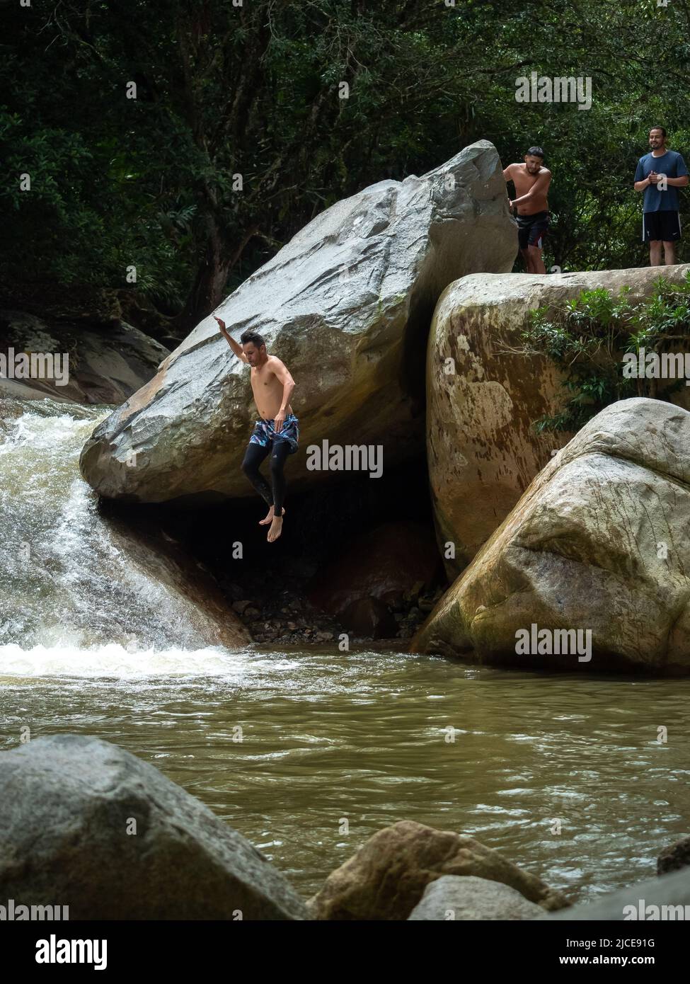 Cisneros, Antioquia, Colombie - 20 février 2022: Homme d'Amérique du Sud qui saute dans la rivière de grands rochers au milieu d'une forêt Banque D'Images