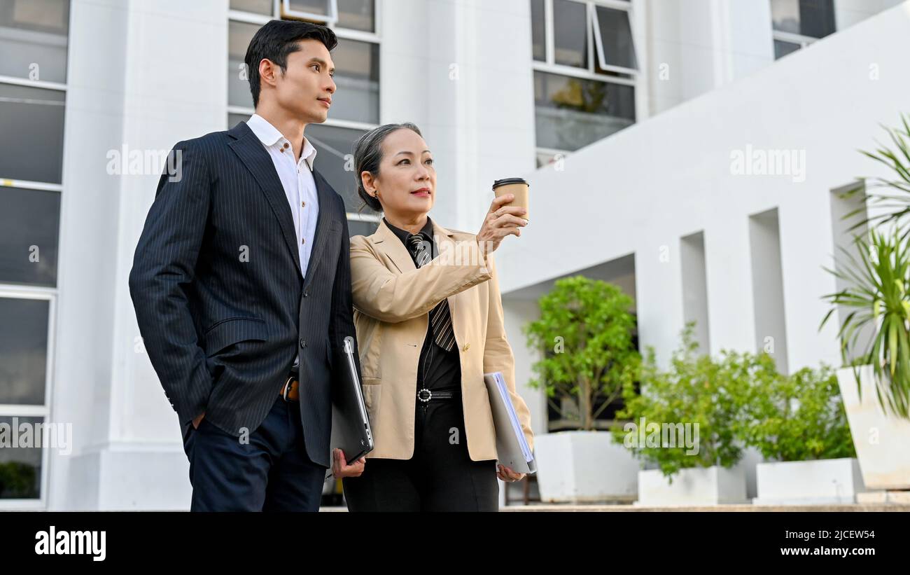 Homme d'affaires asiatique professionnel en costume formel debout à l'extérieur du bâtiment et parlant avec une femme d'affaires âgée ou un cadre supérieur. Banque D'Images