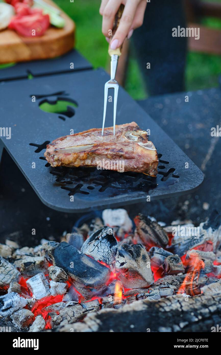 Steak d'os tournant avec fourchette sur la grille du barbecue Banque D'Images