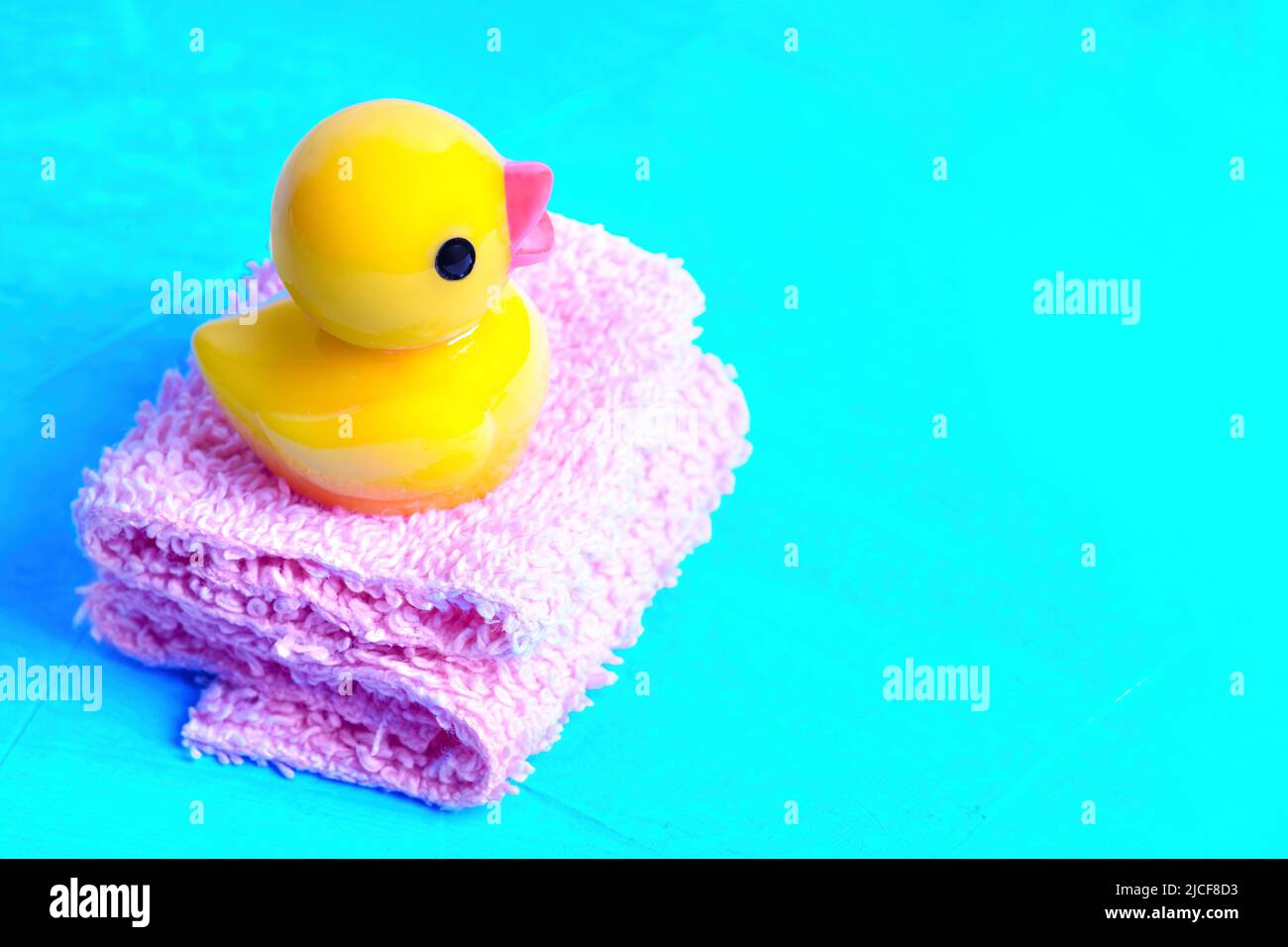 Bébé canard en caoutchouc placé sur une pile de serviettes de bain miniatures isolées sur fond bleu. Concept de bain amusant. Banque D'Images